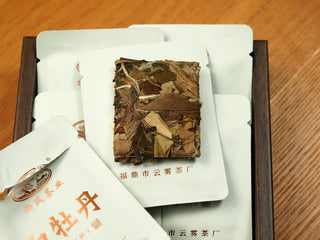 Torn-open wrapper revealing a compressed square tea biscuit of 2018 indoor-withered Fuding White Peony with pressed leaves.