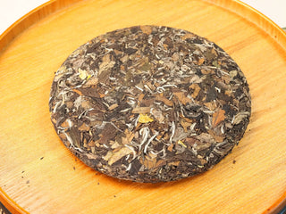 Unwrapped 2020 Fuding Sun-Dried White Peony 350g cake resting on a round wooden tray, showing the pressed leaf and bud surface.