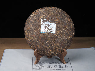 Unwrapped 2021 Dayi Guanchao raw puerh tea cake Batch 2101 on a wooden stand, showing the complete dried tea leaves and inner ticket (neifei).
