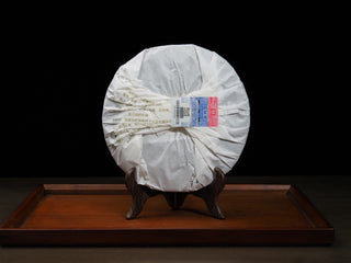2021 Dayi Mi Xiang Raw Puerh tea cake wrapped in traditional white paper, displayed on a wooden stand.
