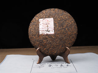 Unwrapped 2022 Dayi 7572 ripe puerh tea cake showing compressed dark brown tea leaves on a wooden stand.
