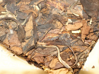 Close-up of 2024 sun-dried Shou Mei and Chen Pi waffle cake surface, dark tea leaves blended with golden tangerine peel strips.