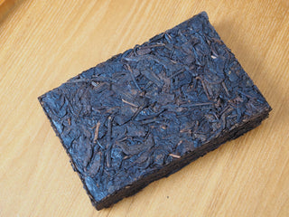 Flat lay view of the unwrapped 2013 Dry-Aged Lincang Ripe Pu-erh tea brick, highlighting its dark, tightly compressed ancient tree tea leaves.