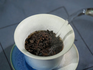 Brewing process of 2006 Liubao tea with hot water being poured into a white ceramic bowl.