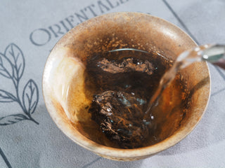 Steaming hot water being poured over Puerh Tea Nuggets in a gaiwan to release the deep amber tea liquor.
