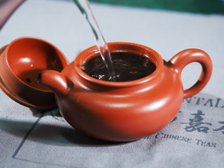 Pouring hot water into a red Yixing clay teapot to brew Vintage Imperial Grade Ripened Puerh tea.
