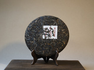 Unwrapped 357g Bulang Mountain Sheng Pu'er tea cake on display stand