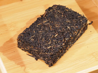 Whole compressed 200g Chang'an Qianqiu Golden Flower Fu Brick Tea on a bamboo tray.