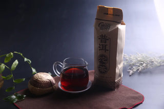 Clear glass pitcher filled with deep red, smooth Lincang Ripe Pu-erh tea liquor on a dark tea mat.