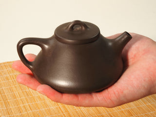 Fengming Ziye Shipiao Yixing teapot held in an open palm, showing the compact 200ml size and low stable profile