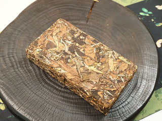 Top view of Gold Brick 2012 sun-dried Fuding White Peony 500g compressed brick, dark brown leaves densely pressed into a firm square brick.