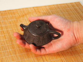 Guyun Shipiao Yixing teapot held in an open palm, showing the small 100ml size and carved antique bronze clay body