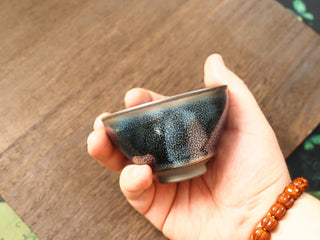 Handheld side view of a Lan Qi Lin Shu Kou Jianzhan bowl, showing the slightly inward-curved rim and the exterior covered in fine silver-blue pinpricks.