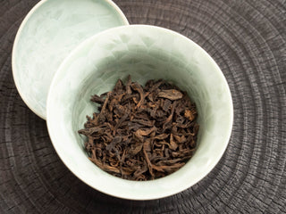Measuring loose leaf ripe pu-erh tea into a celadon gaiwan before brewing.