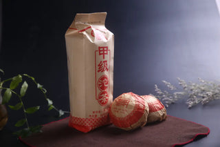 Two compressed bird's nest shape Raw Pu-erh Tuo Cha cakes next to the package.