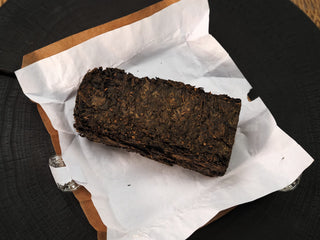 Unwrapped The Little Brick 2018 fu brick tea, a dense dark brown compressed dark tea brick resting on white wrapping paper