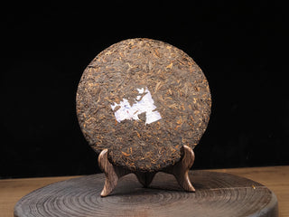 Whole unwrapped 2017 Dayi 7452 ripe puerh tea cake showing a dark, neatly compressed leaf surface on a wooden display stand.
