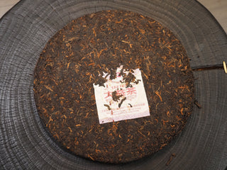 Unwrapped 2019 Dayi 7592 ripe puerh tea cake showing compressed dark brown leaves and the embedded inner trademark ticket (Neifei).