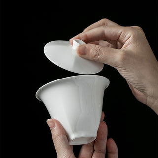 Hand holding a fine white porcelain gaiwan lid during tea preparation