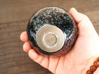 Base of a Wu Zu Bo sky eye oil spot Jianzhan bowl held in hand, showing the unglazed foot ring and a small impressed makers mark.