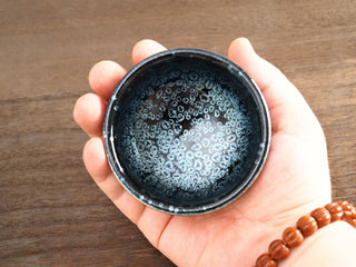 Top view of a Xiang Lu Jianzhan tea bowl held in hand, showing the interior densely covered with silver oil-spot crystals.