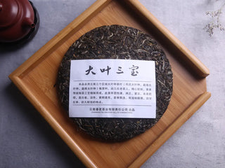 Detailed shot of the Three Legendary Leaves Raw Pu-erh Tea Cake label on a wooden tray.