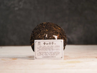 Snow Mountain Rare Wild Ancient Tree Sheng Pu-erh (2016–2023) – 100g Mini Cake, unwrapped with product card, showing the tea cake and detailed texture of leaves