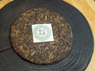 Unwrapped whole cake of 2006 Kaiyuan Reserve aged raw Pu-erh tea showing well-aged compressed tea leaves.