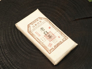 Single 2014 Fuding Shou Mei 100g waffle cake in paper wrapper with Fuding white tea label, red seal and weight marking, top view.