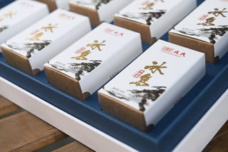 Small white gift box of Mengku Rongshi Bingdao Aged Raw Pu-erh coin cakes with gold calligraphy.
