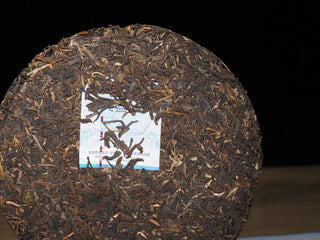 Macro close-up of 2021 Dayi Guanchao raw puerh tea cake surface, showing high-quality dried tea leaves, silver tips, and pressed texture.
