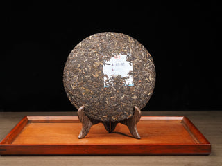 Unwrapped 357g cake of 2021 Dayi Mi Xiang Sheng Puerh tea on a wooden display stand.

