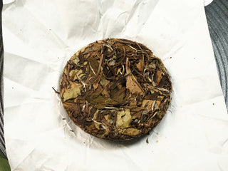 Reverse side of Fortune 2021 sun-dried Fuding Shou Mei 50g mini cake showing the texture of loosely pressed broad leaves.