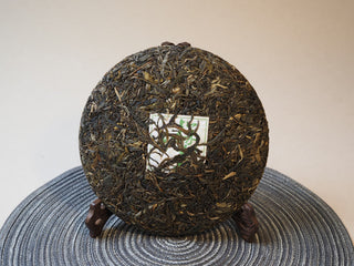 Full view of the compressed 2025 Tan Chun Lincang ancient tree raw Puerh tea cake showing dark leaves.