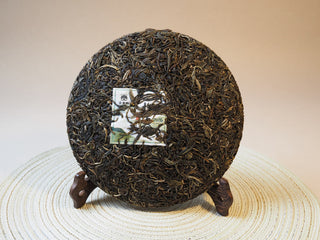 Full view of the compressed 2026 Tan Chun Lincang ancient tree raw Puerh tea cake showing dark leaves.