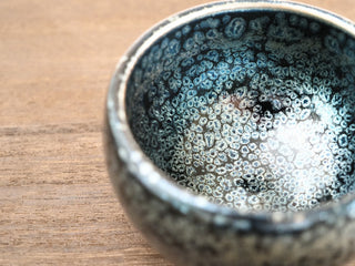 Macro view inside a Bu Dao Weng sky eye oil spot Jianzhan bowl, showing large raised silver crystals with blue-green iridescence.
