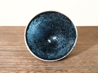 Eye-level front view into a Da Dou Li sky eye oil spot Jianzhan bowl, showing the wide flared rim, the steep conical interior, and densely packed silver-blue crystals.