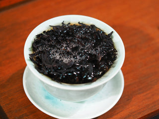 Deeply roasted Da Hong Pao tea leaves steeping in hot water, revealing rich aroma.