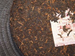 Close-up of 2019 Dayi 7592 ripe puerh tea cake surface, highlighting the embedded Menghai Tea Factory trademark ticket.