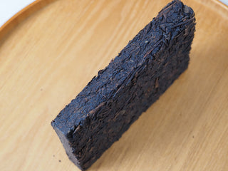 Side profile view of the 2013 Lincang Rpc Pu-erh Ancient Tree Tea Brick on a wooden tray, showing the thickness and density of the compressed brick.