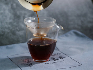 Filtering the deep amber Liubao tea infusion into a glass pitcher for a clean brew.