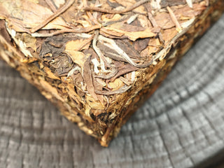 Corner of the Gold Brick 2012 Fuding White Peony brick showing tightly compressed dark leaves with silvery buds and tea stems.
