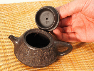 Hand lifting the lid of a Guyun Shipiao Yixing teapot, showing the lid underside seals and sandy clay texture