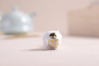 A single hand-rolled Yunnan white tea dragon pearl wrapped in protective white tissue paper.