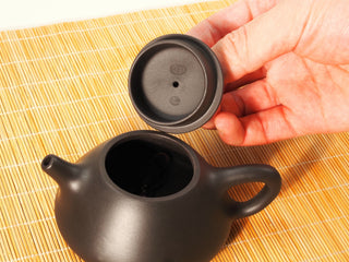 Hand lifting the lid of a Black Zhu Ni Ziye Shipiao Yixing teapot, showing the maker's seal stamp inside the lid