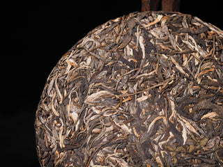 Macro view of unwrapped Lao Man'e ancient tree raw Puerh cake surface showing the thick, hand-selected leaves and natural colors.