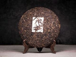 Front side of unwrapped 2019 Lincang Ancient Arbor Sheng Pu-erh Tea Cake showing glossy compressed tea leaves and silver buds