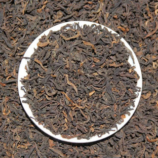 Top view of loose leaf ripe puerh tea mixed with dried rose petals on a white ceramic plate.