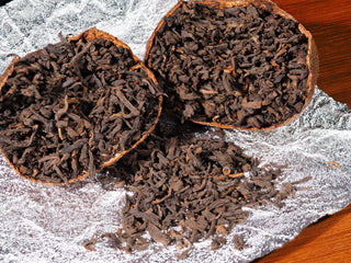 Premium loose Menghai ripe Pu-erh tea leaves displayed next to dried Xinhui Chenpi citrus shell.