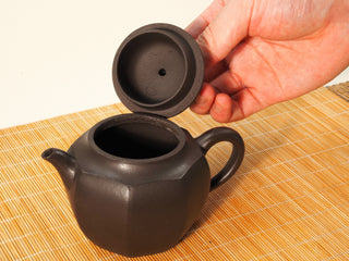 Hand lifting lid of Shihuang Bafang Yixing teapot, revealing inner lid air hole and open mouth, on bamboo mat